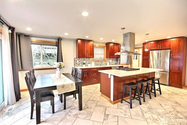 kitchen featuring island range hood, decorative light fixtures, stainless steel appliances, light countertops, and a sink