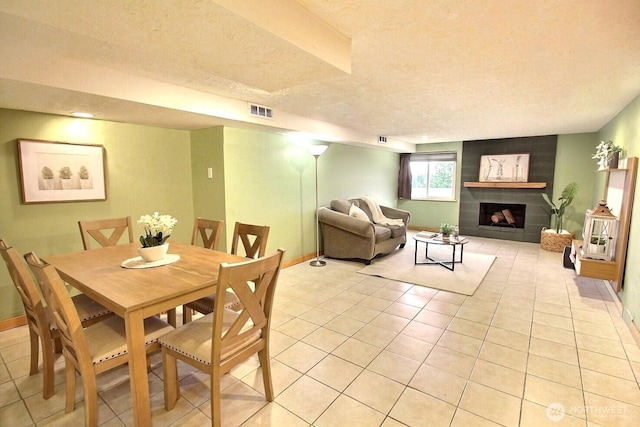 dining space featuring a textured ceiling, light tile patterned flooring, a tiled fireplace, and visible vents