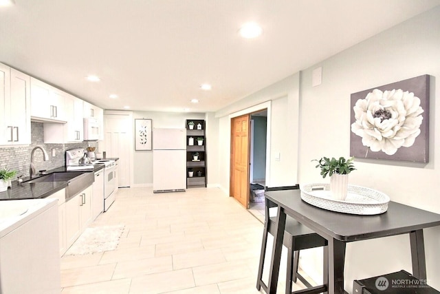 kitchen with white appliances, a sink, white cabinetry, backsplash, and dark countertops