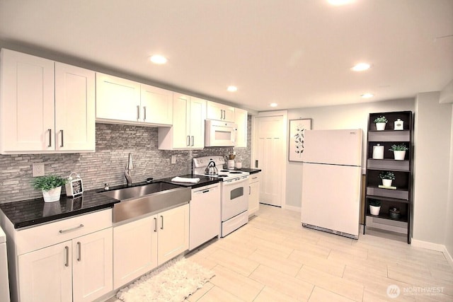 kitchen featuring dark countertops, backsplash, white cabinetry, a sink, and white appliances