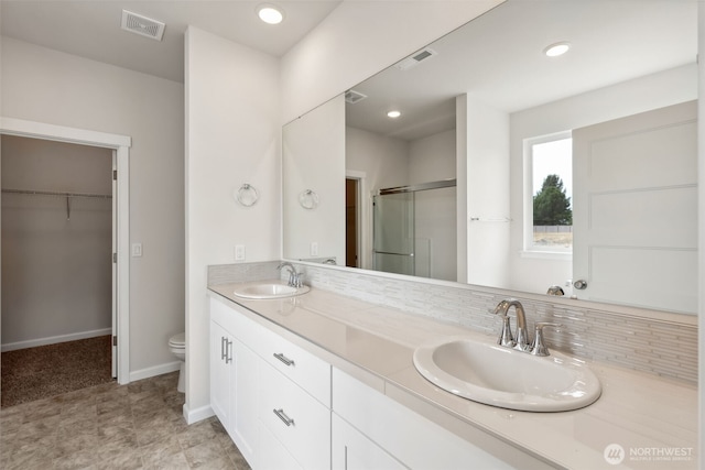 bathroom featuring a stall shower, visible vents, a walk in closet, and a sink