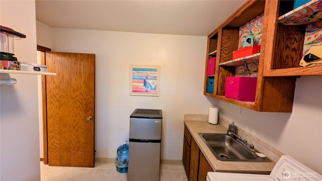 kitchen featuring light tile patterned floors, a sink, freestanding refrigerator, open shelves, and washer / clothes dryer