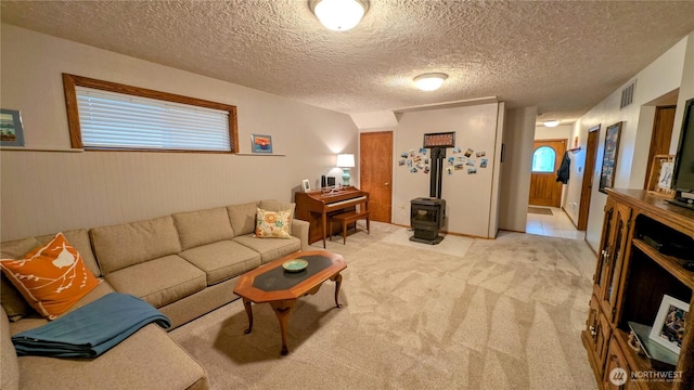 living area featuring a wood stove, light colored carpet, visible vents, and a textured ceiling