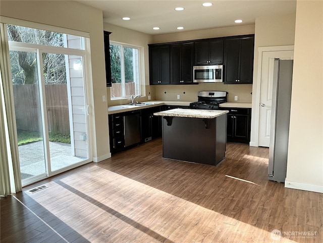 kitchen featuring a breakfast bar, wood finished floors, a kitchen island, visible vents, and appliances with stainless steel finishes