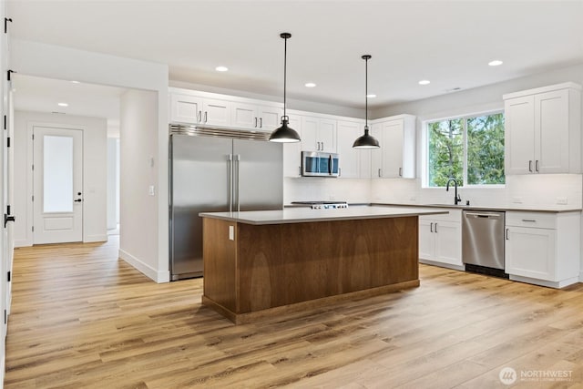 kitchen with appliances with stainless steel finishes, white cabinetry, decorative light fixtures, and a center island