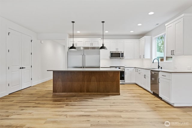 kitchen with a center island, decorative light fixtures, stainless steel appliances, light countertops, and white cabinets