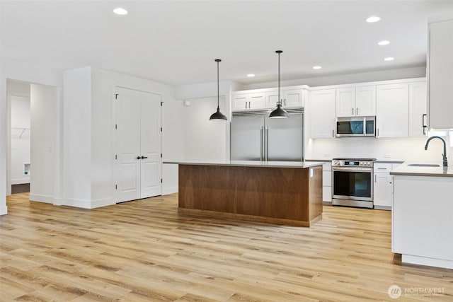 kitchen featuring a kitchen island, white cabinetry, hanging light fixtures, appliances with stainless steel finishes, and light countertops