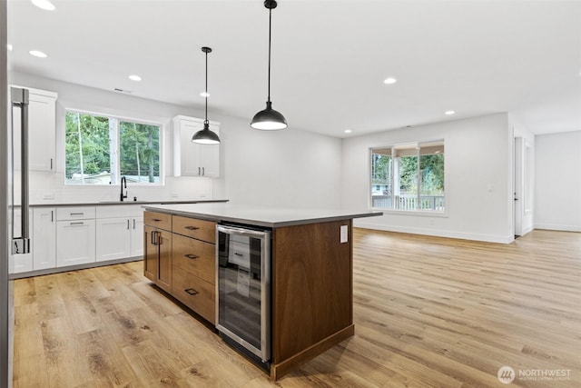 kitchen featuring wine cooler, a kitchen island, white cabinets, hanging light fixtures, and light countertops