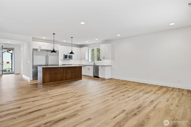 kitchen featuring a kitchen island, appliances with stainless steel finishes, open floor plan, hanging light fixtures, and white cabinetry