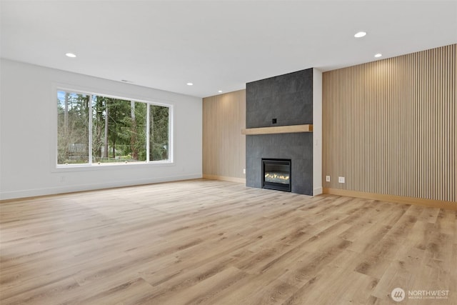 unfurnished living room featuring baseboards, a tile fireplace, light wood-style flooring, and recessed lighting