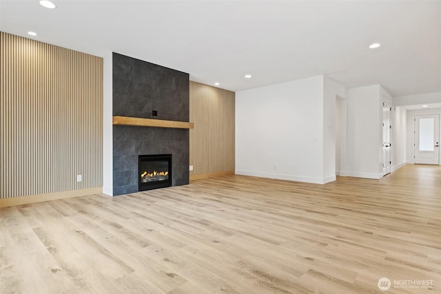 unfurnished living room with light wood-type flooring, baseboards, a tile fireplace, and recessed lighting