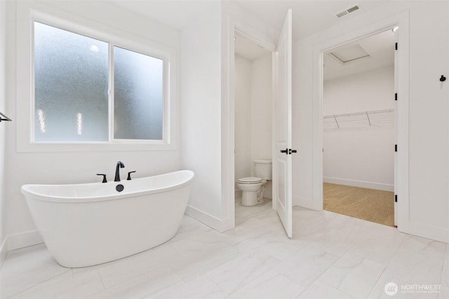 bathroom with a freestanding tub, toilet, visible vents, marble finish floor, and a walk in closet