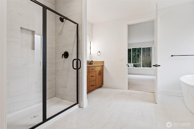 full bath with baseboards, a freestanding bath, a shower stall, and vanity