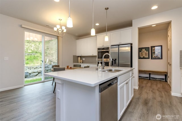 kitchen with a center island with sink, decorative light fixtures, stainless steel appliances, light countertops, and white cabinetry