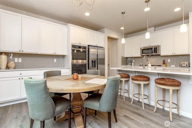 kitchen with light countertops, hanging light fixtures, appliances with stainless steel finishes, white cabinetry, and a sink