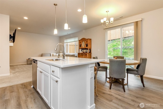 kitchen featuring a sink, white cabinetry, light countertops, hanging light fixtures, and an island with sink