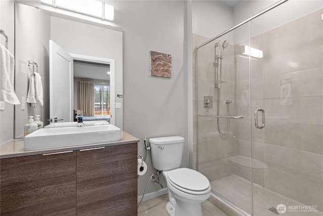 bathroom with a stall shower, vanity, toilet, and baseboards