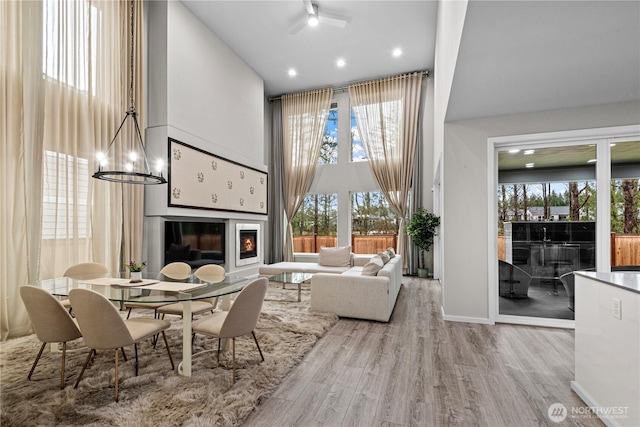 interior space featuring baseboards, a glass covered fireplace, a towering ceiling, wood finished floors, and a chandelier