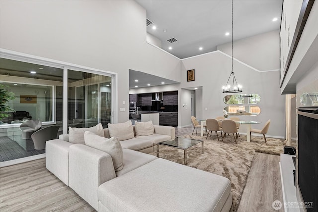 living room with recessed lighting, visible vents, a towering ceiling, wood finished floors, and a chandelier