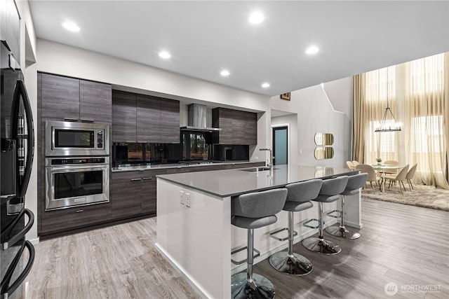 kitchen with wall chimney exhaust hood, modern cabinets, appliances with stainless steel finishes, and a sink