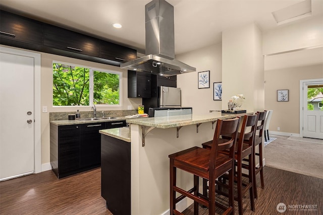11752 35th Ave NE, Seattle, WA 98125 - kitchen with island exhaust hood, dark cabinetry, a sink, a breakfast bar, and baseboards