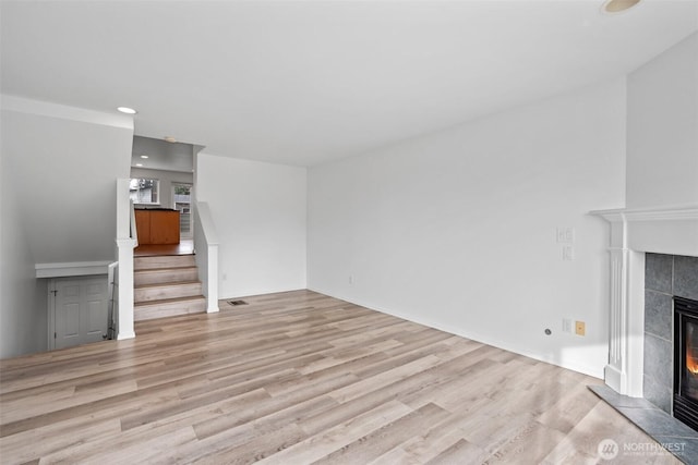 unfurnished living room featuring light wood-style floors, recessed lighting, stairway, and a tiled fireplace