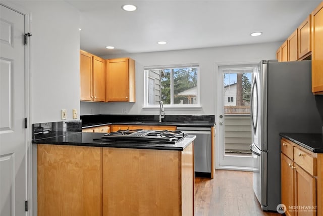 kitchen with dark countertops, appliances with stainless steel finishes, a sink, light wood-type flooring, and a peninsula