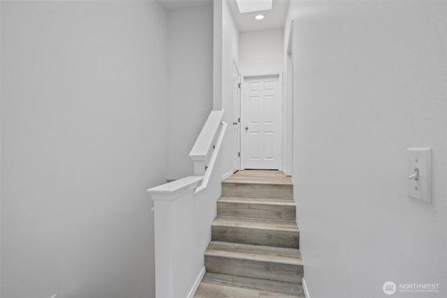 stairway with a skylight, wood finished floors, and baseboards