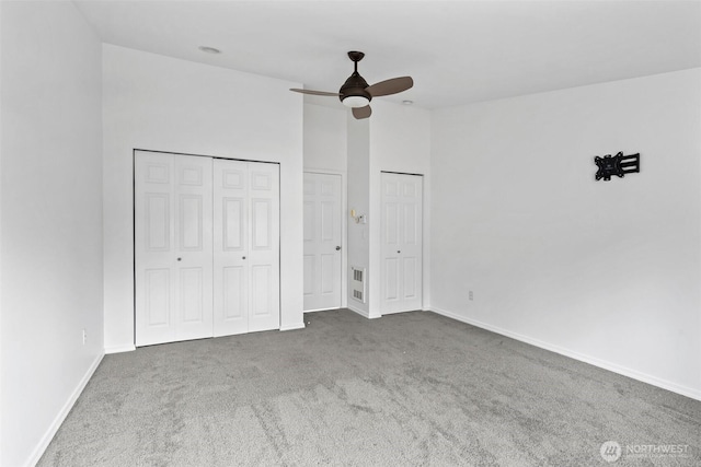 unfurnished bedroom featuring ceiling fan, carpet floors, visible vents, baseboards, and two closets