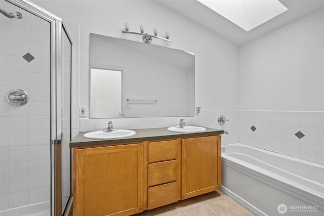 full bath with a skylight, a sink, tile patterned floors, double vanity, and a stall shower