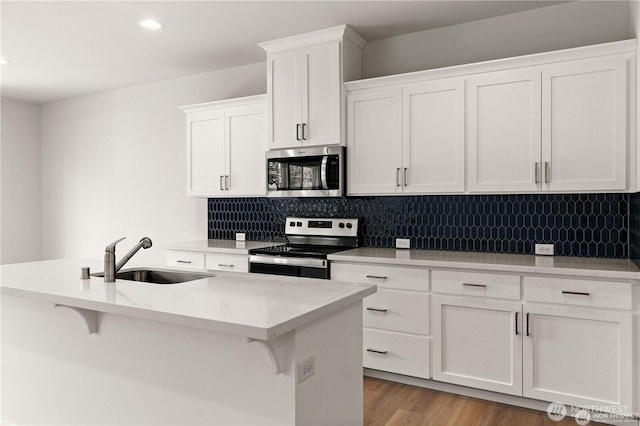 kitchen featuring a sink, white cabinetry, appliances with stainless steel finishes, tasteful backsplash, and a kitchen bar