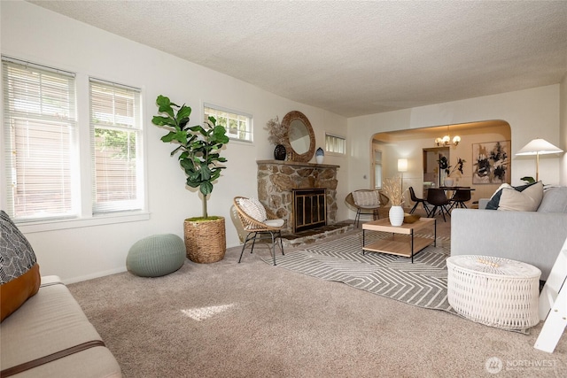 carpeted living room with an inviting chandelier, a fireplace, arched walkways, and a textured ceiling