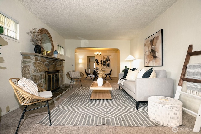 carpeted living area featuring arched walkways, a notable chandelier, a fireplace, and a textured ceiling