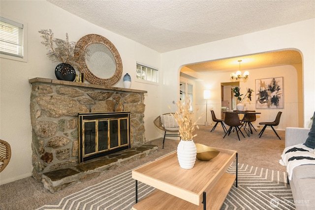 carpeted living area with an inviting chandelier, arched walkways, a textured ceiling, and a stone fireplace