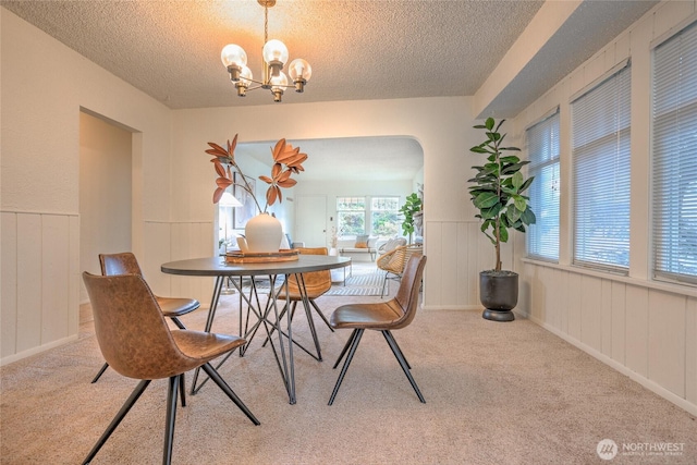 carpeted dining area with arched walkways, a wainscoted wall, a notable chandelier, and a textured ceiling