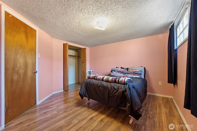 bedroom with a textured ceiling, wood finished floors, and baseboards