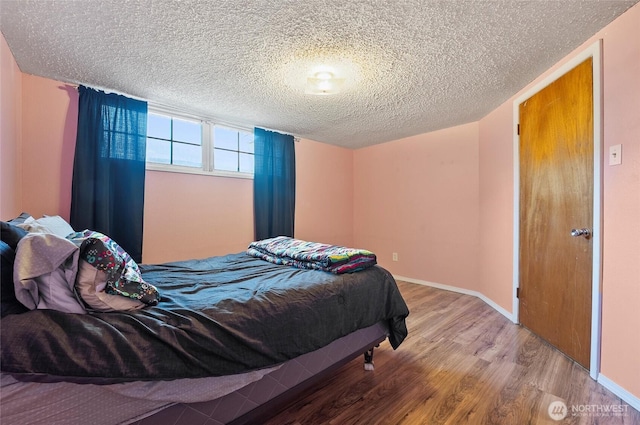 bedroom featuring a textured ceiling, wood finished floors, and baseboards