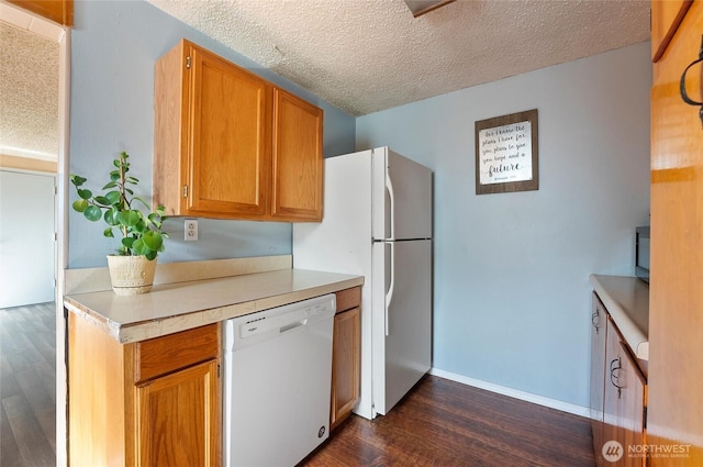 kitchen with a textured ceiling, white appliances, baseboards, light countertops, and dark wood finished floors