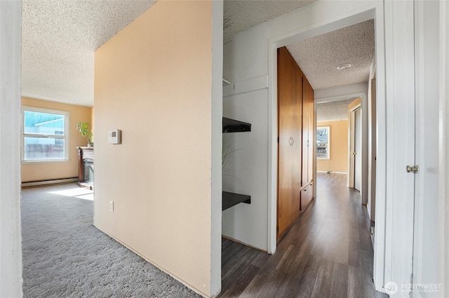 corridor featuring a textured ceiling, dark wood-style flooring, baseboard heating, and dark colored carpet