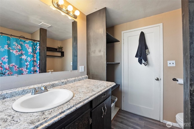 bathroom featuring toilet, visible vents, wood finished floors, and vanity