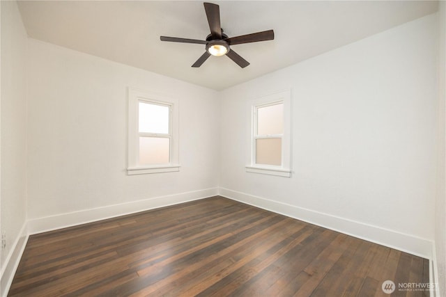 spare room featuring dark wood-style flooring, a ceiling fan, and baseboards