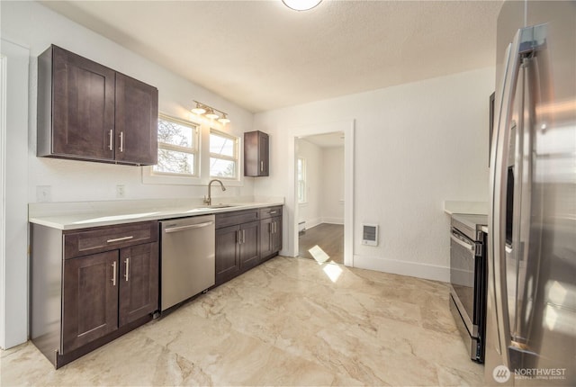 kitchen with light countertops, appliances with stainless steel finishes, a sink, and dark brown cabinets