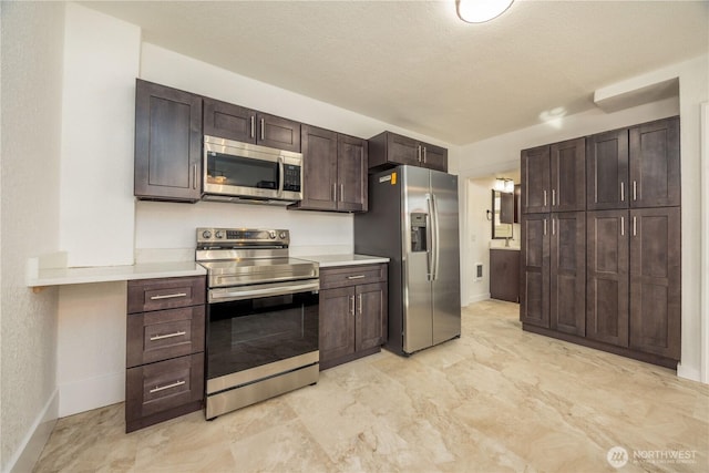 kitchen with stainless steel appliances, light countertops, a textured ceiling, dark brown cabinets, and baseboards