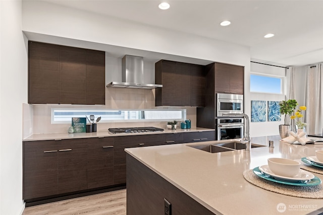 kitchen with dark brown cabinetry, stainless steel appliances, light countertops, wall chimney exhaust hood, and modern cabinets