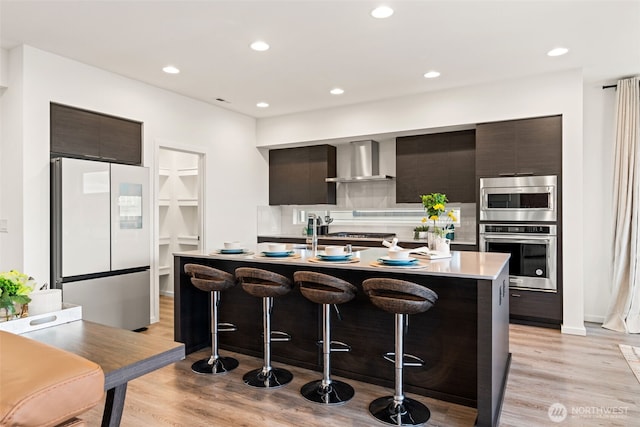 kitchen with a breakfast bar, light wood-style floors, freestanding refrigerator, wall chimney exhaust hood, and modern cabinets