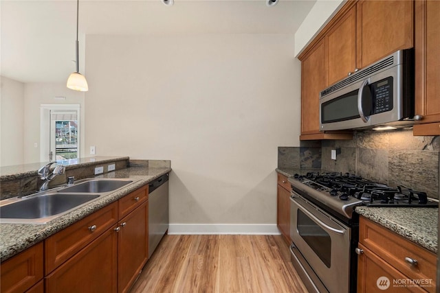 kitchen featuring decorative backsplash, appliances with stainless steel finishes, brown cabinets, pendant lighting, and a sink