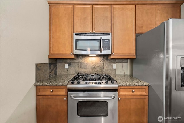 kitchen with dark stone counters, appliances with stainless steel finishes, brown cabinets, and tasteful backsplash