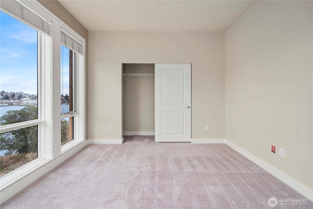 unfurnished bedroom featuring light carpet, baseboards, and a closet