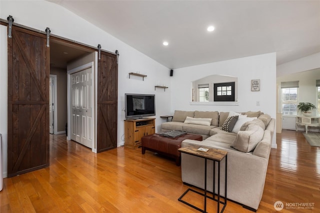 living room featuring lofted ceiling, a barn door, light wood-type flooring, and recessed lighting