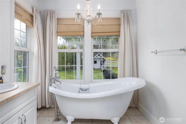 bathroom featuring baseboards, tile patterned flooring, vanity, a freestanding tub, and a chandelier